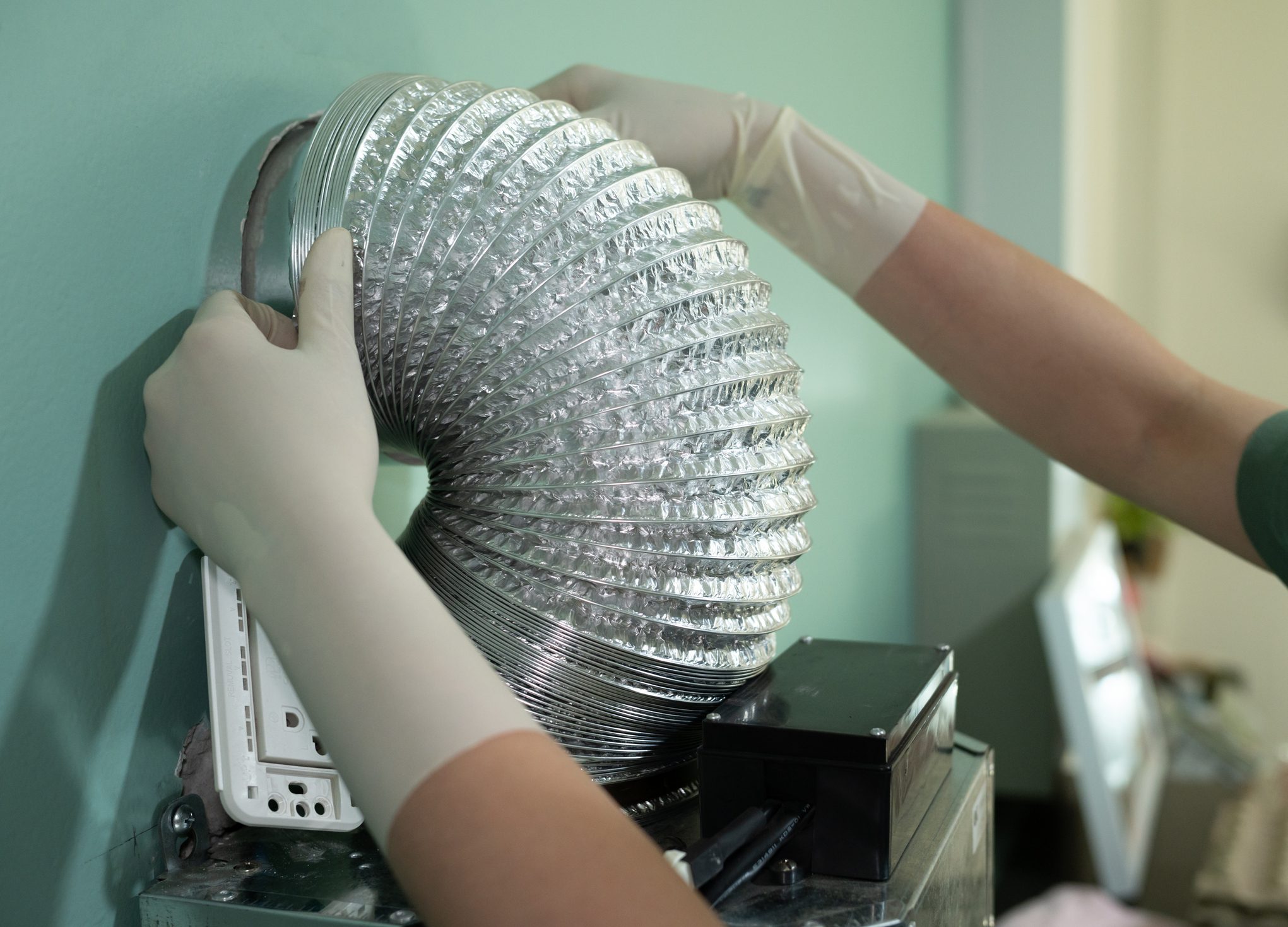 Gloved hands installing a flexible duct tube.